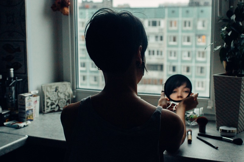 The woman is making makeup, there is a reflection of her in the mirror